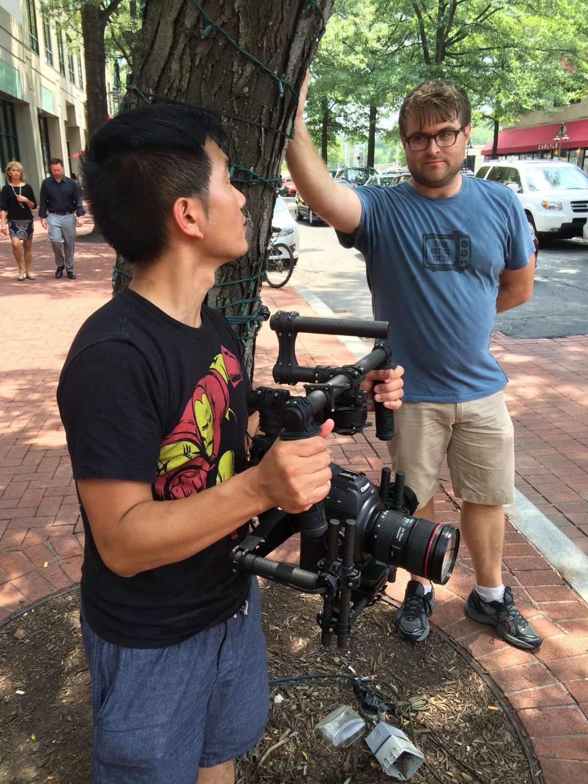 Our camera operator holding a Canon cinema camera on a gimbal on a brick sidewalk, a crew member beside him